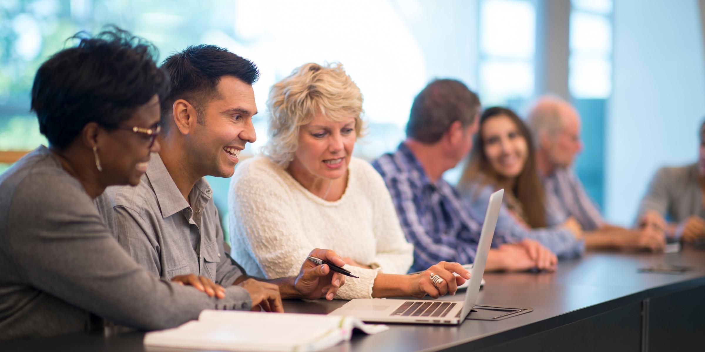 a group of adults smiling as they work together at a table with laptops