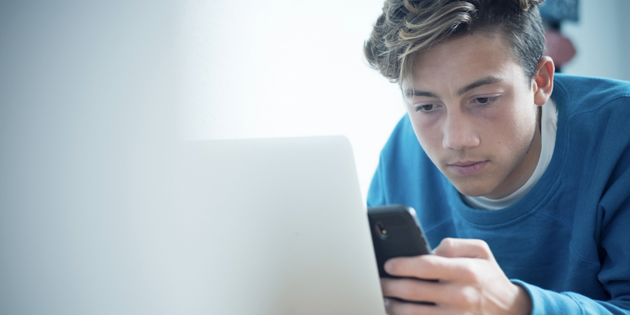 teenager looking at a cell phone and a laptop screen