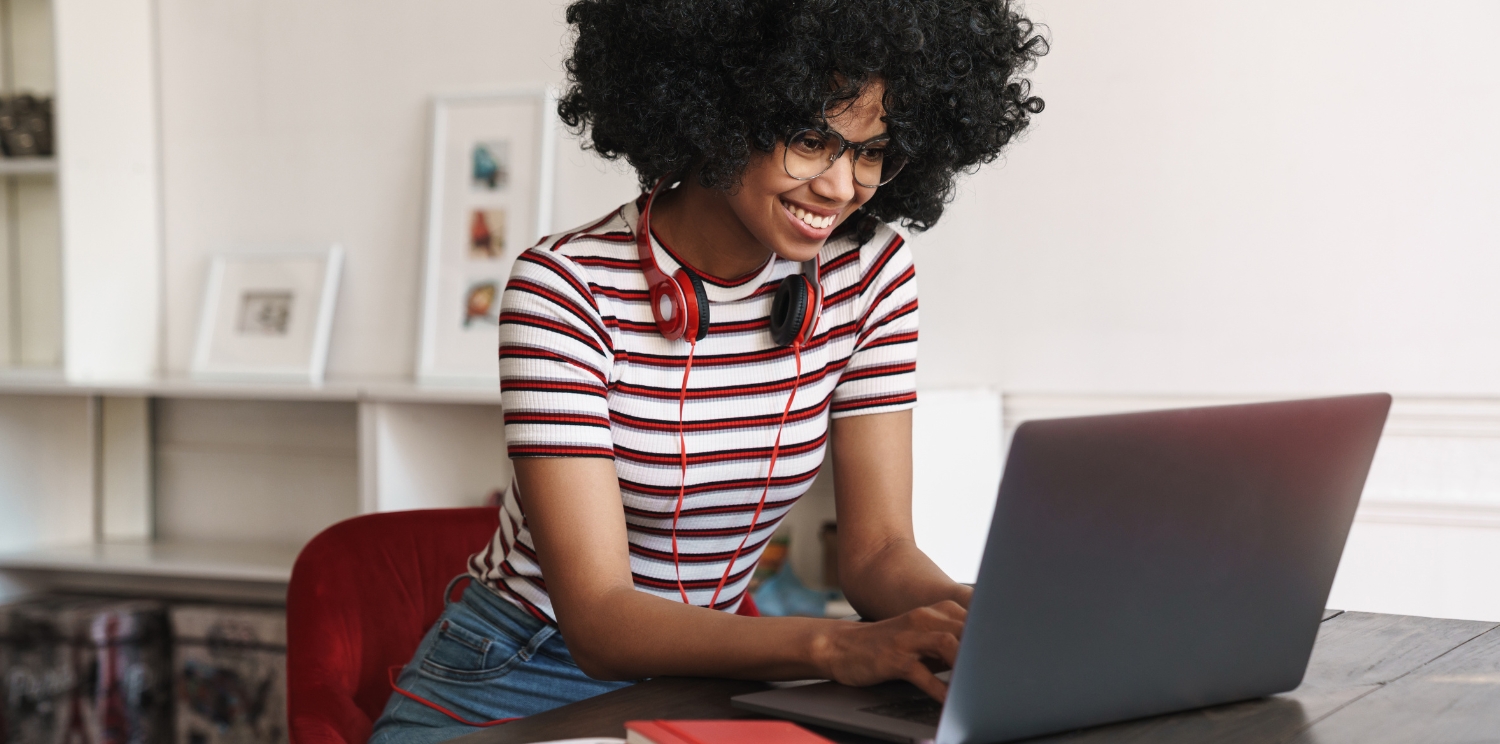 a student smiling at a laptop and wearing headphones